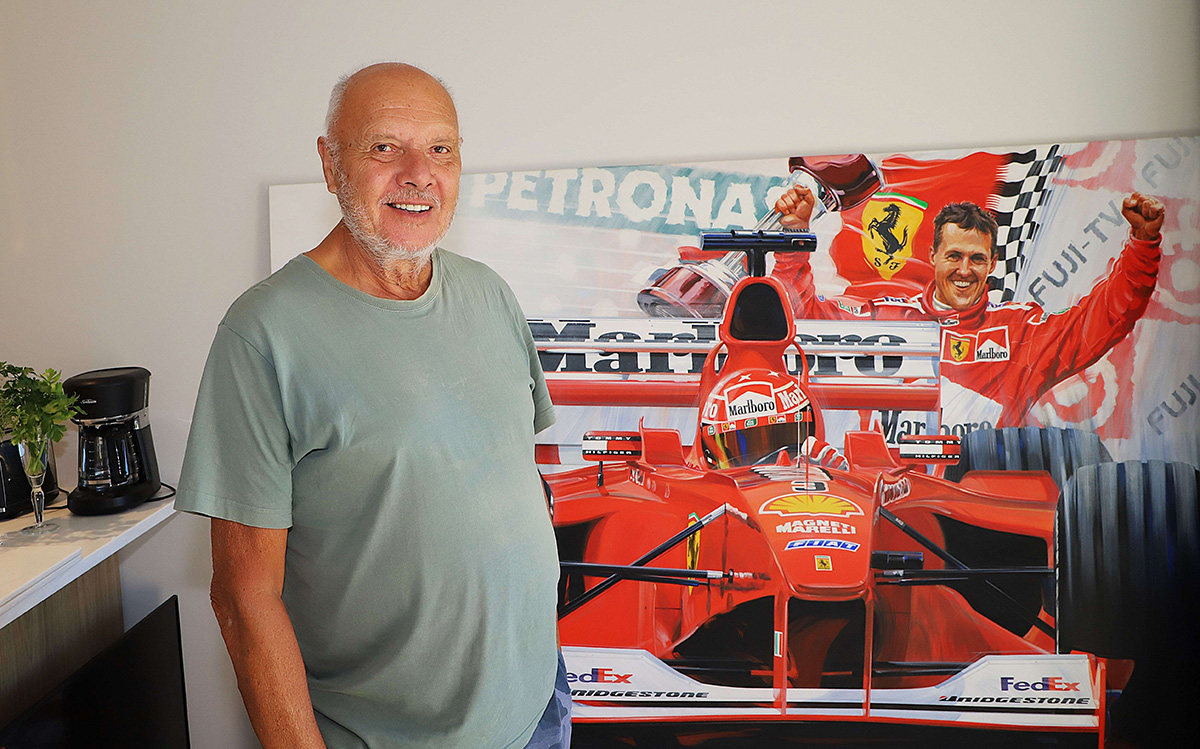 Older man stands in a living room with a giant canvas painting of Michael Schumacher and his racing car in the background